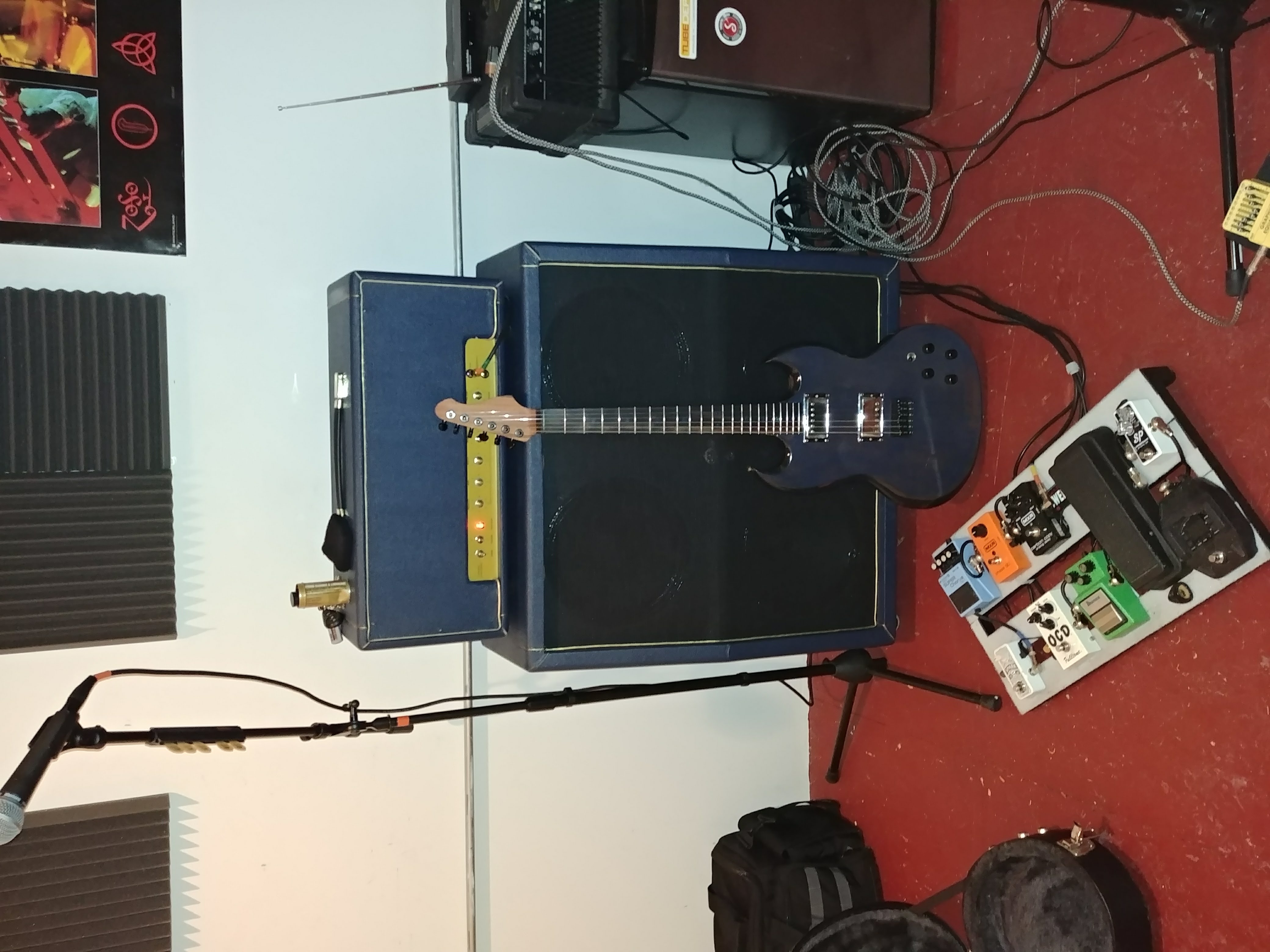 Finished blue electric guitar leaning on the homebuilt amplifier in a band rehearsal room